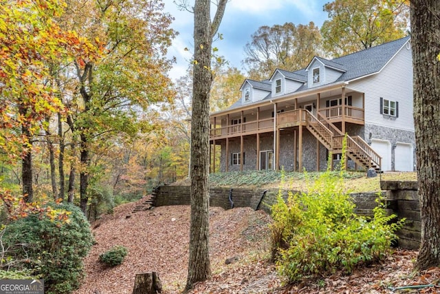 back of property featuring a garage, stone siding, and stairs