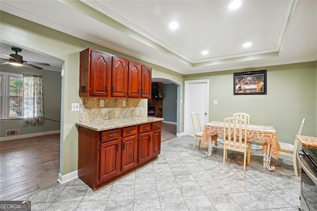 kitchen featuring tasteful backsplash, ornamental molding, light hardwood / wood-style floors, a tray ceiling, and ceiling fan