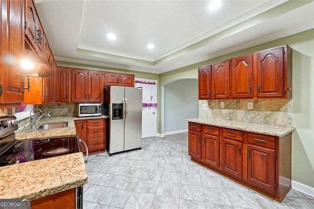 kitchen with sink, light stone counters, appliances with stainless steel finishes, backsplash, and a tray ceiling