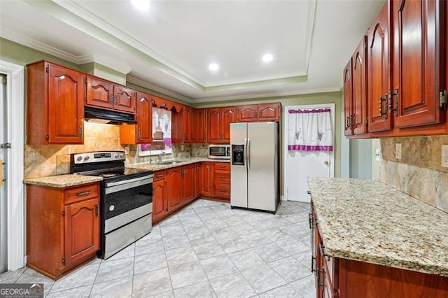 kitchen with stainless steel appliances, a raised ceiling, light stone counters, and backsplash