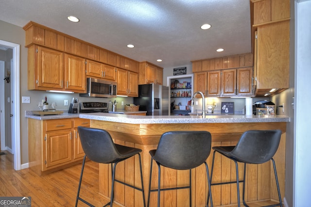 kitchen with stainless steel appliances, a textured ceiling, light hardwood / wood-style flooring, and kitchen peninsula