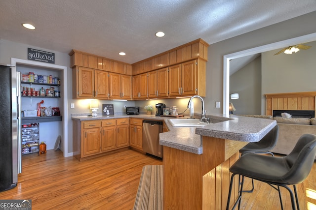 kitchen with kitchen peninsula, a textured ceiling, light wood-type flooring, and appliances with stainless steel finishes