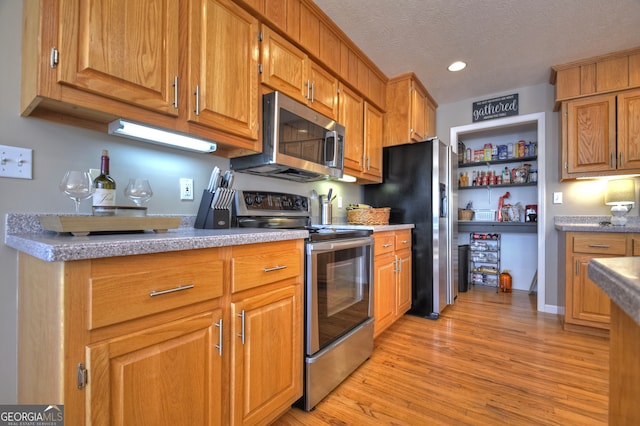 kitchen featuring a textured ceiling, light wood-type flooring, and appliances with stainless steel finishes