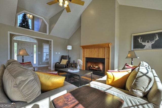 living room featuring a warm lit fireplace, ceiling fan, baseboards, and high vaulted ceiling