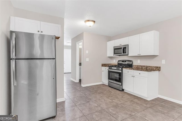 kitchen with dark stone counters, appliances with stainless steel finishes, light tile patterned flooring, and white cabinets