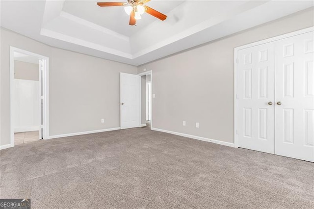 unfurnished bedroom with ceiling fan, a closet, carpet floors, and a tray ceiling