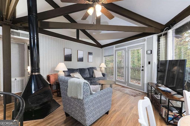 living room featuring light wood-type flooring, a wood stove, ceiling fan, and vaulted ceiling with beams