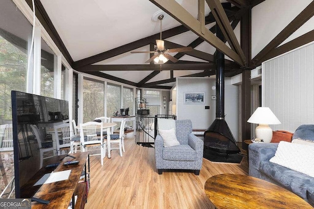 living room with lofted ceiling with beams, light wood-type flooring, a wood stove, and ceiling fan