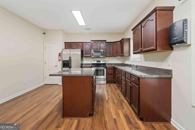 kitchen featuring appliances with stainless steel finishes, dark brown cabinets, dark hardwood / wood-style flooring, sink, and a center island