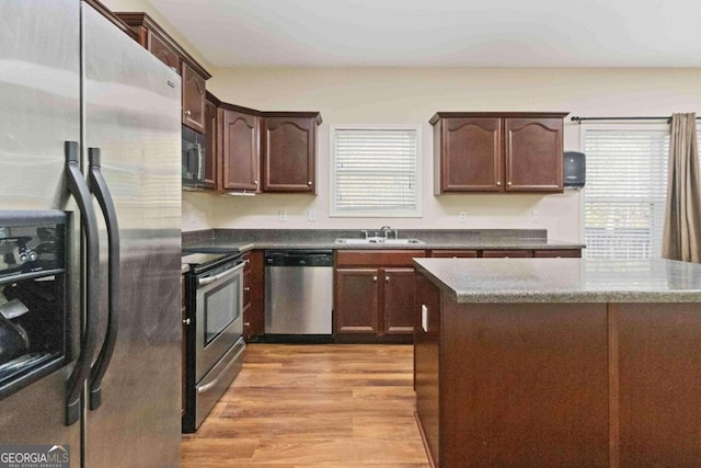 kitchen with appliances with stainless steel finishes, dark brown cabinetry, sink, dark stone countertops, and light hardwood / wood-style flooring