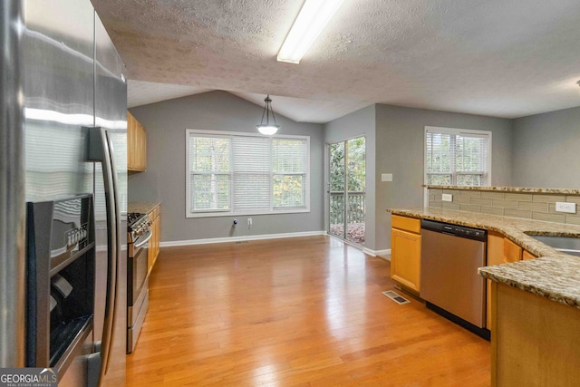 kitchen with stainless steel appliances, lofted ceiling, a textured ceiling, light hardwood / wood-style flooring, and decorative light fixtures