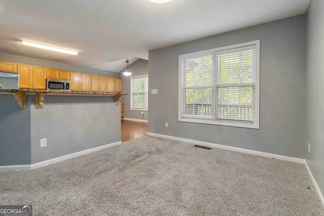 kitchen featuring a kitchen bar, stainless steel appliances, lofted ceiling, hanging light fixtures, and light brown cabinets