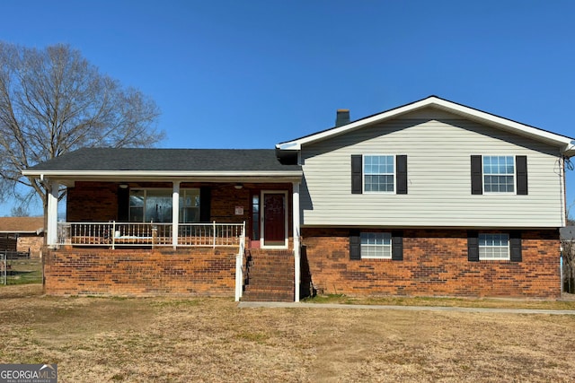 tri-level home featuring a chimney, a porch, and brick siding