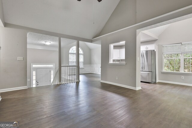 unfurnished living room featuring high vaulted ceiling, plenty of natural light, dark wood-type flooring, and a textured ceiling