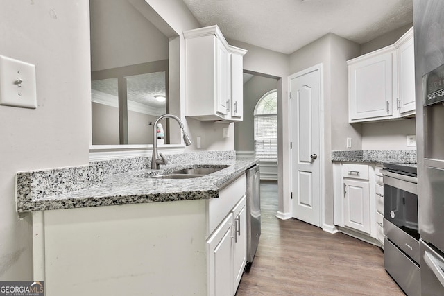 kitchen with sink, a textured ceiling, hardwood / wood-style floors, stone counters, and white cabinets