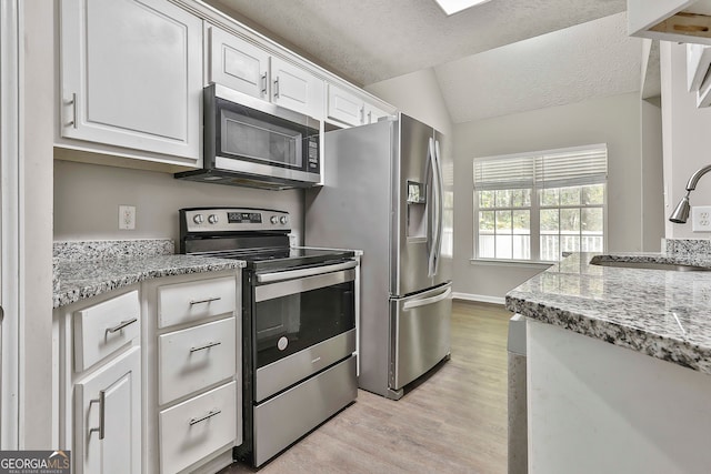 kitchen featuring vaulted ceiling, light hardwood / wood-style flooring, sink, white cabinetry, and appliances with stainless steel finishes