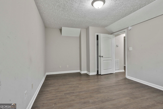 interior space with dark wood-type flooring, a textured ceiling, and vaulted ceiling