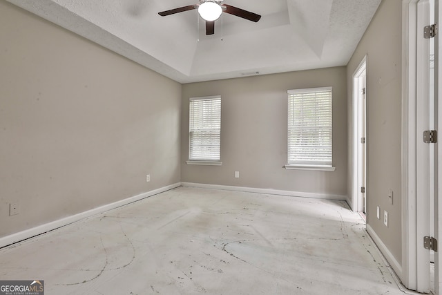 empty room with ceiling fan, a textured ceiling, and a raised ceiling