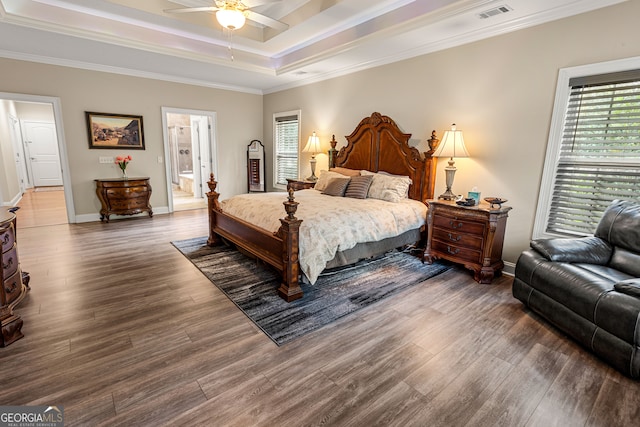 bedroom with dark wood-type flooring, connected bathroom, ornamental molding, ceiling fan, and a tray ceiling