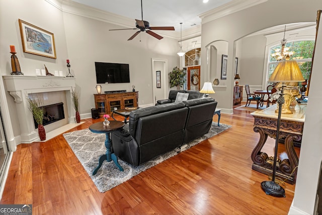 living room featuring crown molding, ceiling fan with notable chandelier, a premium fireplace, and light hardwood / wood-style flooring