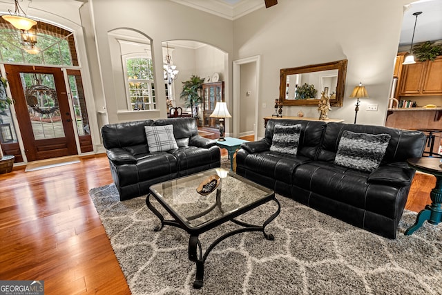 living room featuring an inviting chandelier, a towering ceiling, ornamental molding, and light hardwood / wood-style flooring