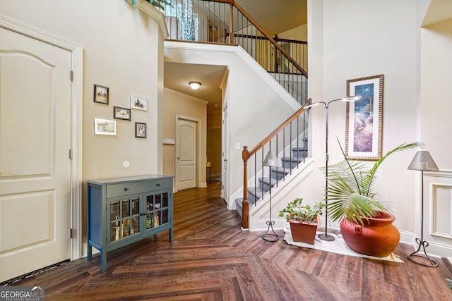 foyer featuring a towering ceiling, crown molding, and dark parquet floors