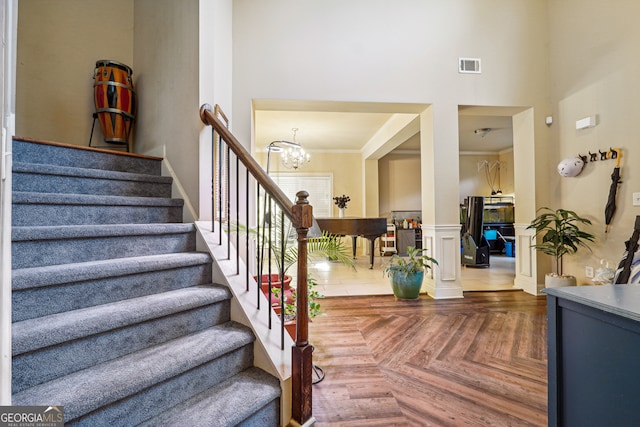 stairway with a towering ceiling, a chandelier, parquet floors, and ornamental molding