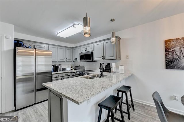 kitchen featuring kitchen peninsula, appliances with stainless steel finishes, backsplash, light hardwood / wood-style flooring, and pendant lighting