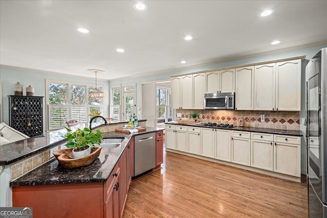 kitchen with sink, appliances with stainless steel finishes, ornamental molding, pendant lighting, and light wood-type flooring