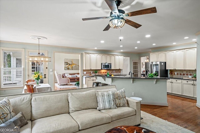 living room featuring ornamental molding, ceiling fan with notable chandelier, and wood-type flooring