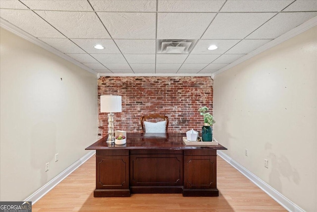 unfurnished office featuring ornamental molding, a drop ceiling, light hardwood / wood-style floors, and brick wall