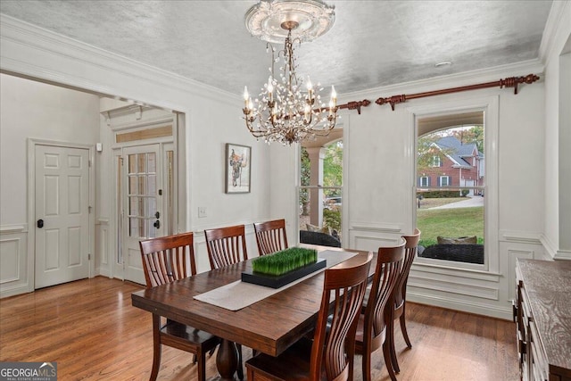 dining area with a textured ceiling, wood-type flooring, a notable chandelier, and crown molding