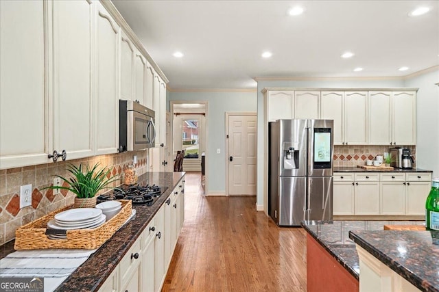 kitchen featuring stainless steel appliances, dark stone counters, decorative backsplash, crown molding, and light hardwood / wood-style flooring