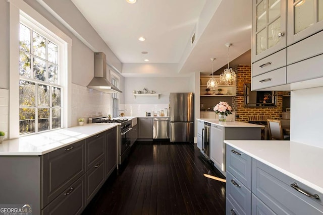 kitchen featuring stainless steel appliances, wall chimney exhaust hood, decorative light fixtures, dark wood-type flooring, and gray cabinetry