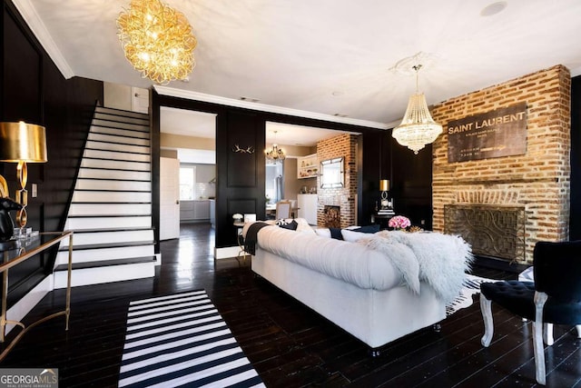 living room featuring dark hardwood / wood-style flooring, a chandelier, crown molding, a fireplace, and brick wall