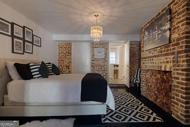 bedroom with a chandelier, brick wall, and dark hardwood / wood-style flooring