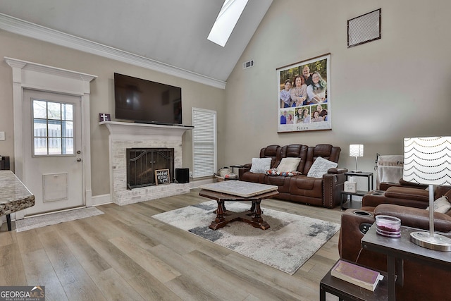 living room with a brick fireplace, light hardwood / wood-style floors, ornamental molding, high vaulted ceiling, and a skylight