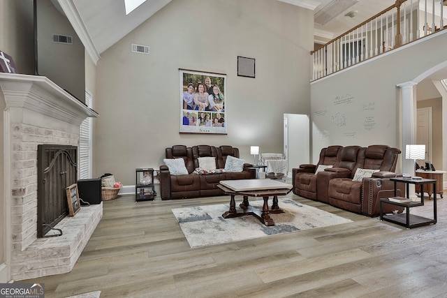 living room featuring high vaulted ceiling, ornate columns, light hardwood / wood-style floors, and a fireplace