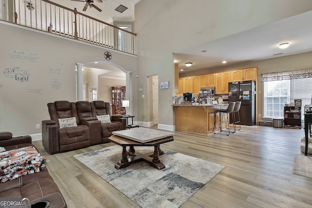 living room featuring a high ceiling, ceiling fan, light hardwood / wood-style flooring, and decorative columns