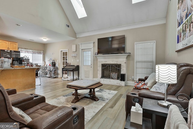 living room featuring ornamental molding, a fireplace, high vaulted ceiling, a skylight, and light wood-type flooring