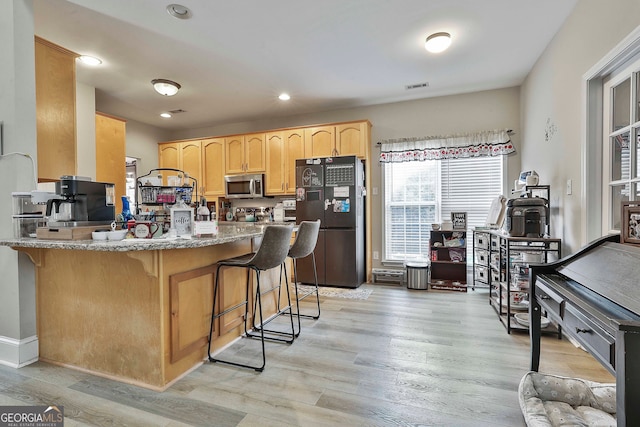 kitchen with black refrigerator, kitchen peninsula, a breakfast bar area, light wood-type flooring, and light brown cabinetry