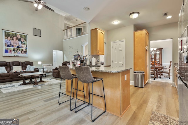 kitchen with light brown cabinets, a towering ceiling, light hardwood / wood-style floors, and light stone countertops