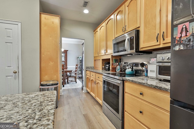 kitchen with light brown cabinets, light wood-type flooring, stainless steel appliances, and dark stone counters