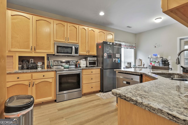 kitchen with appliances with stainless steel finishes, light brown cabinetry, sink, and light hardwood / wood-style flooring