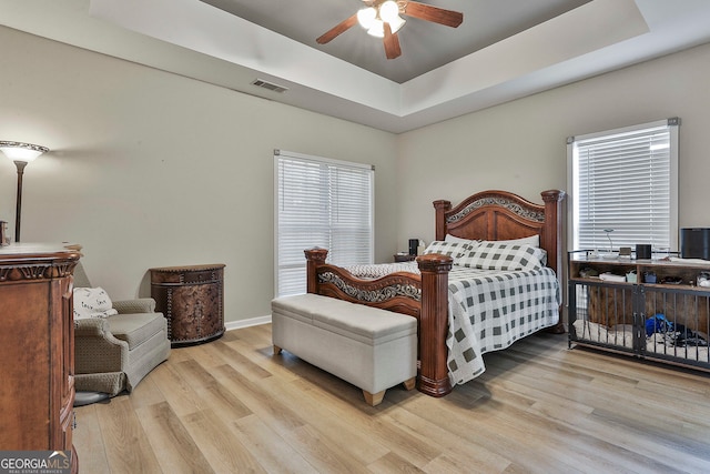 bedroom featuring ceiling fan, light wood-type flooring, and a tray ceiling