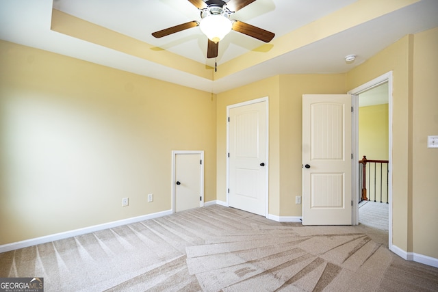 unfurnished bedroom with a tray ceiling, ceiling fan, and carpet floors