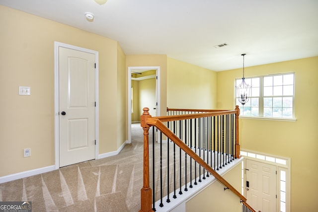 hallway with light colored carpet and an inviting chandelier