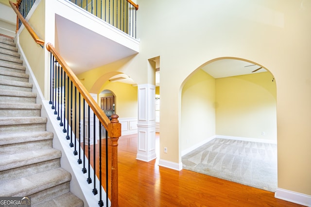 stairs featuring a towering ceiling, hardwood / wood-style floors, and decorative columns