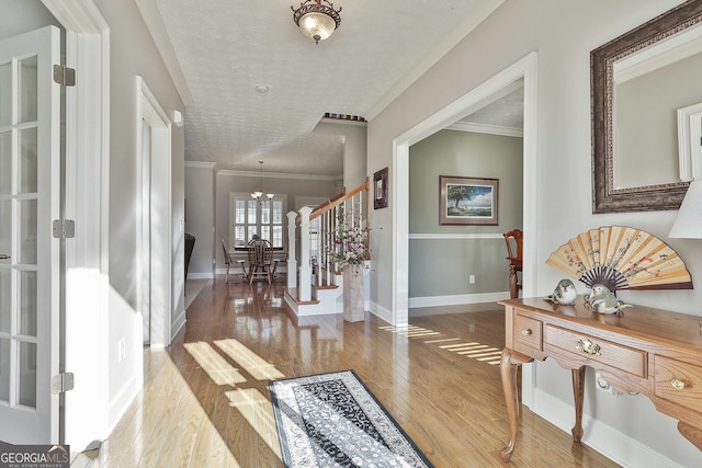 foyer with light wood finished floors, a textured ceiling, baseboards, and ornamental molding