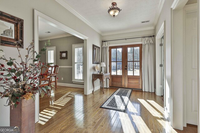 entrance foyer featuring french doors, a wealth of natural light, light hardwood / wood-style floors, and crown molding